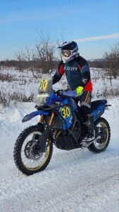 Спортсмен на синьому мотоциклі долає засніжену трасу під час чемпіонату з кантрі кросу в Кіровоградській області