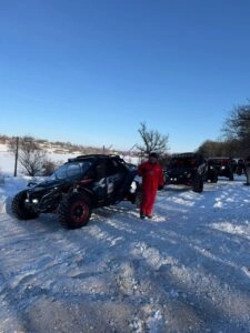 Учасник у червоному костюмі біля баггі на засніженій трасі під час чемпіонату з кантрі кросу в Кіровоградській області