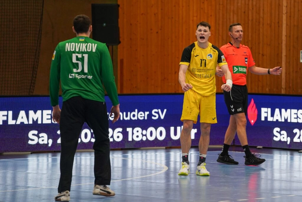 Гандболіст у жовтій формі обговорює гру з воротарем у зеленій формі на майданчику під час матчу
