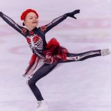 Юна фігуристка в яскравому костюмі виконує елемент на льоду під час змагань в Одесі