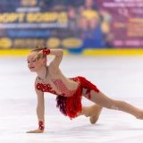 Юна фігуристка у яскравому костюмі виконує елемент на льоду під час змагань в Одесі