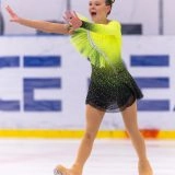 Юна фігуристка в яскравій сукні виконує елемент на льоду під час змагань в Одесі