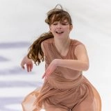 Юна фігуристка виконує елемент на льоду під час змагань в Одесі, демонструючи емоції та майстерність