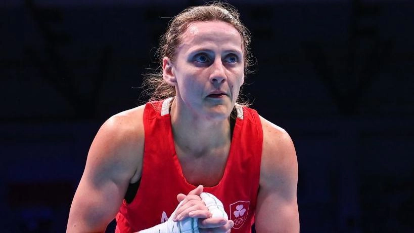 Жінка-боксер у червоній формі на рингу під час змагань, зосереджено дивиться вперед