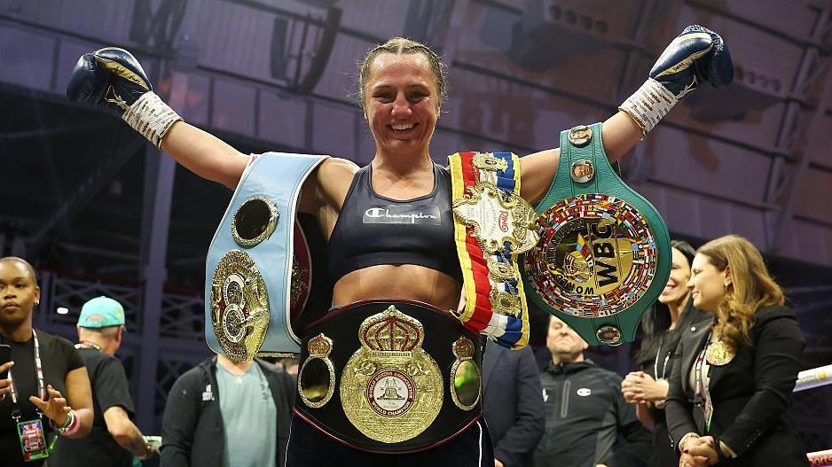 Боксерка з піднятими руками та чемпіонськими поясами після перемоги на рингу в Лондоні