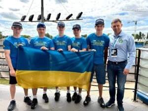 Група молодих людей у синіх футболках тримає український прапор на відкритому повітрі